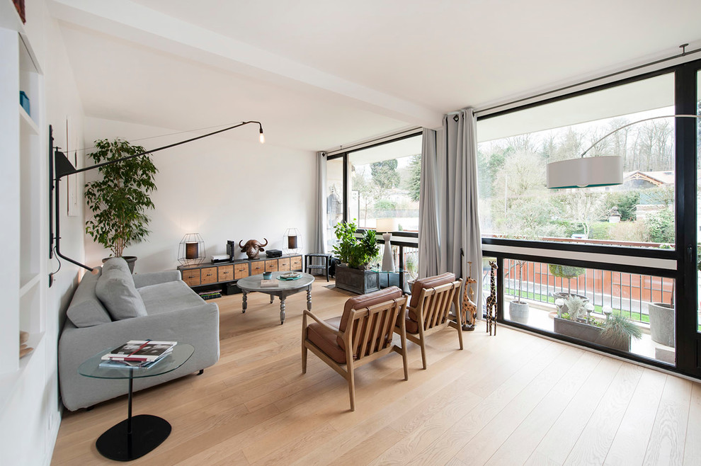 This is an example of a large contemporary formal open concept living room in Paris with white walls, light hardwood floors, no fireplace and no tv.