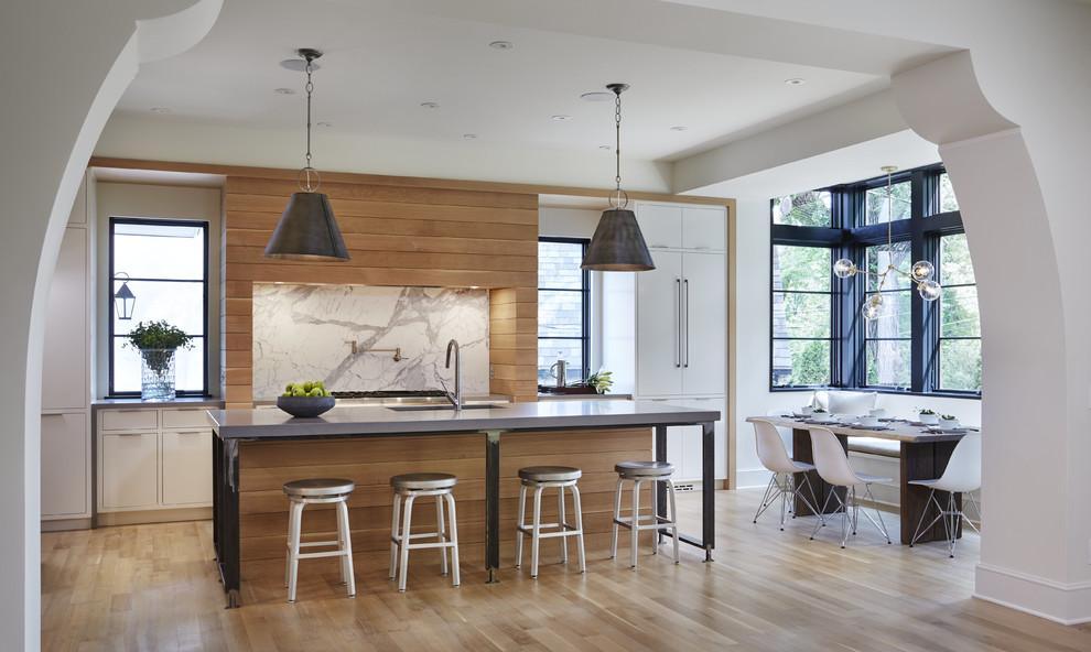 Photo of a contemporary galley eat-in kitchen in Minneapolis with an undermount sink, flat-panel cabinets, white cabinets, white splashback, light hardwood floors, with island, solid surface benchtops, stone slab splashback and panelled appliances.