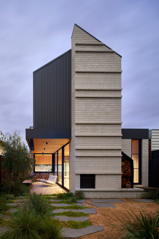 Cette image montre une petite façade de maison grise design en brique à un étage avec un toit à deux pans, un toit en métal et un toit noir.