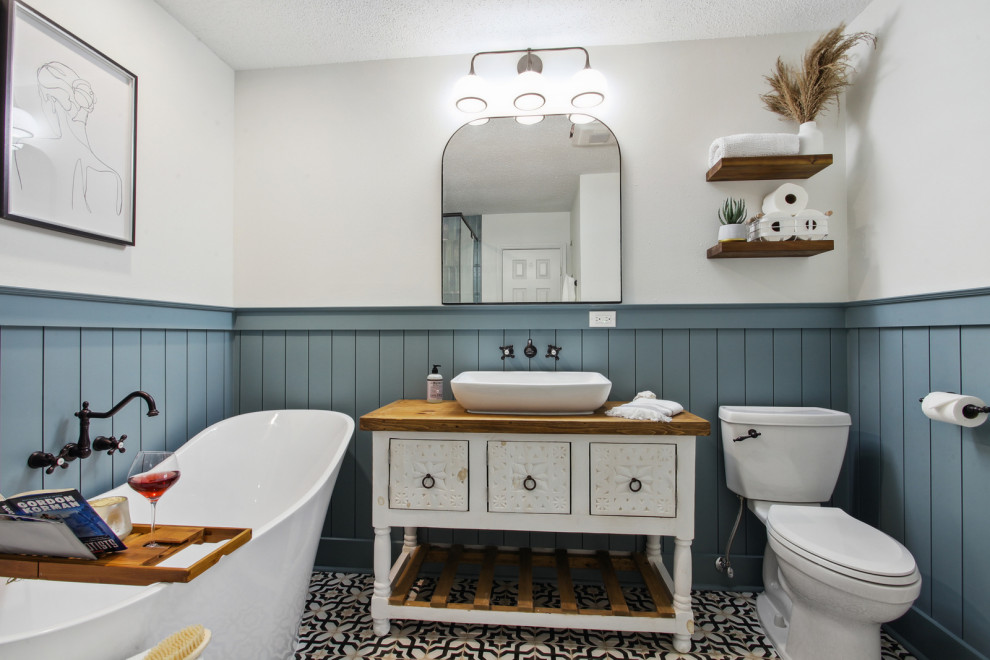 Пример оригинального дизайна: главная ванная комната среднего размера с фасадами островного типа, искусственно-состаренными фасадами, отдельно стоящей ванной, угловым душем, раздельным унитазом, синей плиткой, керамической плиткой, синими стенами, полом из керамической плитки, настольной раковиной, столешницей из дерева, черным полом, душем с распашными дверями, коричневой столешницей, нишей, тумбой под одну раковину, напольной тумбой и стенами из вагонки