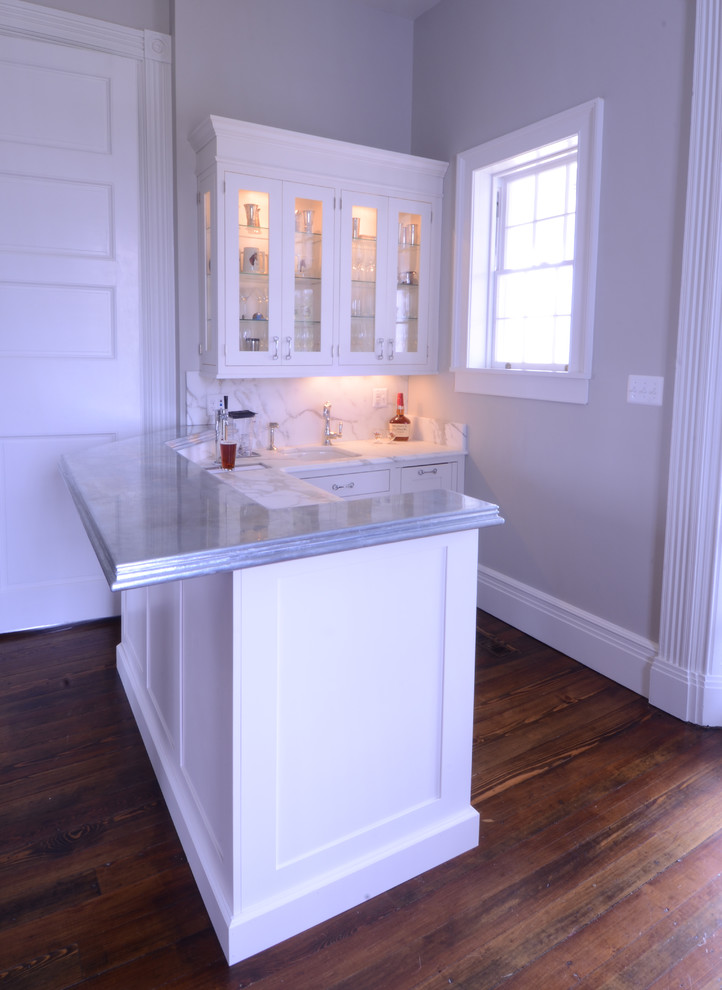 Design ideas for a mid-sized transitional l-shaped wet bar in Baltimore with an undermount sink, shaker cabinets, white cabinets, marble benchtops, white splashback, stone slab splashback, dark hardwood floors and brown floor.