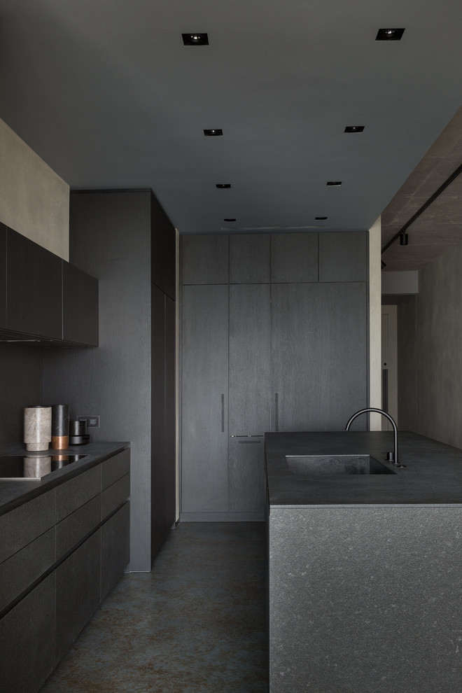 Mid-sized contemporary l-shaped open plan kitchen in Moscow with an integrated sink, flat-panel cabinets, black cabinets, granite benchtops, black splashback, stone slab splashback, black appliances, concrete floors, with island, blue floor and black benchtop.