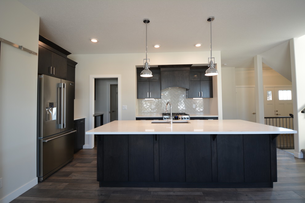 Example of a mid-sized transitional single-wall dark wood floor and brown floor open concept kitchen design in Calgary with an undermount sink, flat-panel cabinets, dark wood cabinets, quartz countertops, white backsplash, porcelain backsplash, stainless steel appliances and an island