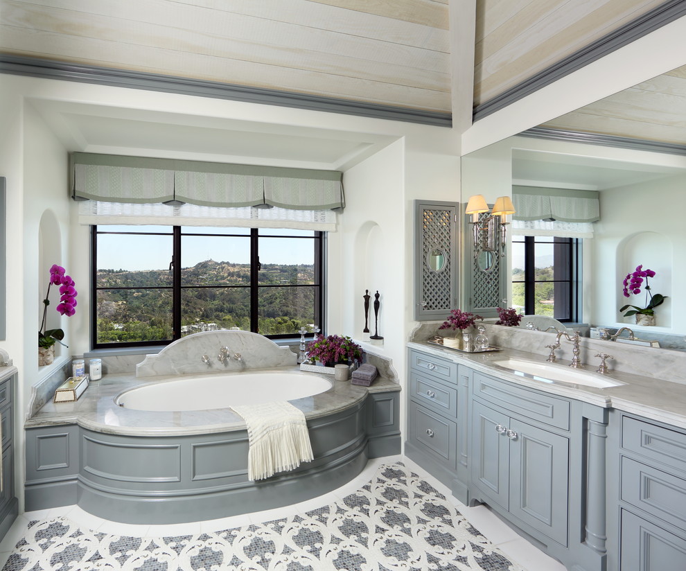 Design ideas for a mediterranean master bathroom in Los Angeles with beaded inset cabinets, grey cabinets, an undermount tub, white walls, an undermount sink and multi-coloured floor.