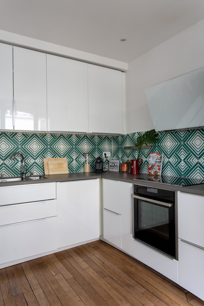 This is an example of a mid-sized midcentury u-shaped separate kitchen in Paris with an undermount sink, beaded inset cabinets, white cabinets, quartzite benchtops, green splashback, cement tile splashback, black appliances, medium hardwood floors, no island and grey benchtop.