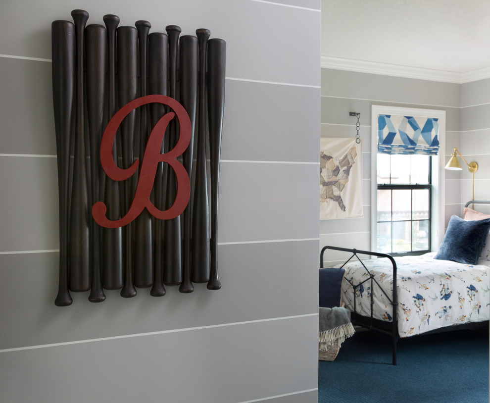 Future Baseball Player - A custom wall decoration was created out of 1/2 bats and embellished with the little boy's initial. The handmade fabric wall hanging depicts the USA in neutral tones.  A classic iron bed with vintage baseball bedding carries the baseball them in the space.  Blue and white roman shades add a punch of color.  Two toned stripes with a white banding wrap the room. Brass wall lights create the perfect place to read in bed.