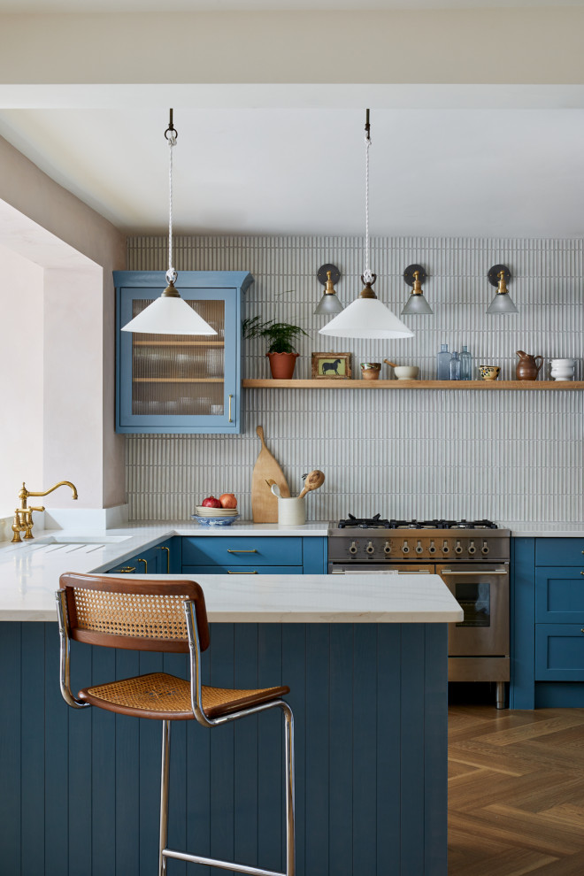 Bild på ett vintage vit vitt kök, med en undermonterad diskho, skåp i shakerstil, blå skåp, bänkskiva i kvarts, grått stänkskydd, rostfria vitvaror, mellanmörkt trägolv, en halv köksö och brunt golv