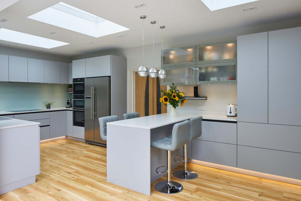 Inspiration for a mid-sized contemporary u-shaped eat-in kitchen in London with flat-panel cabinets, grey cabinets, quartzite benchtops, green splashback, glass sheet splashback, stainless steel appliances, a peninsula and white benchtop.