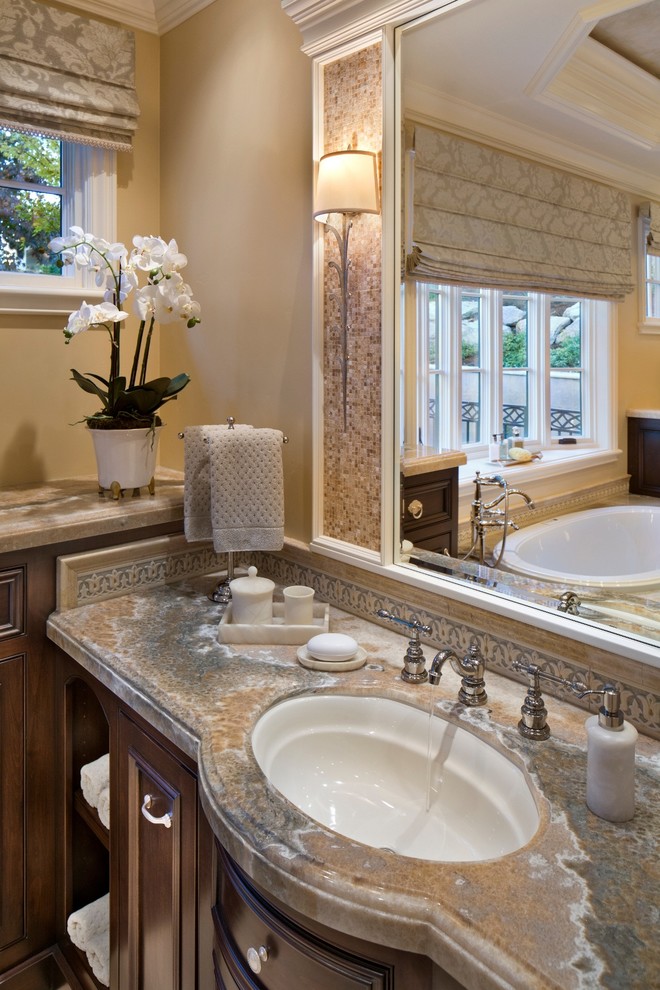 This is an example of a traditional bathroom in San Francisco with dark wood cabinets, a drop-in tub and an undermount sink.