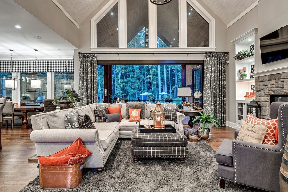 Example of a large classic open concept medium tone wood floor and brown floor family room design in New York with gray walls, a standard fireplace, a stone fireplace and a wall-mounted tv