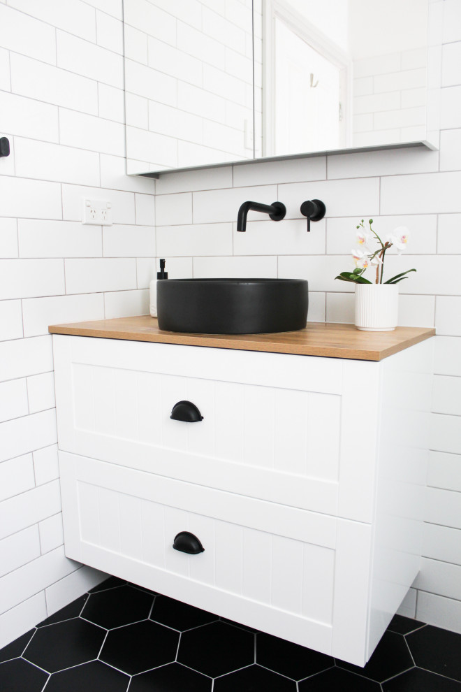 Design ideas for a small modern kids bathroom in Perth with shaker cabinets, white cabinets, an open shower, a one-piece toilet, white tile, ceramic tile, white walls, porcelain floors, a vessel sink, wood benchtops, black floor, an open shower, beige benchtops, a single vanity, a floating vanity and brick walls.