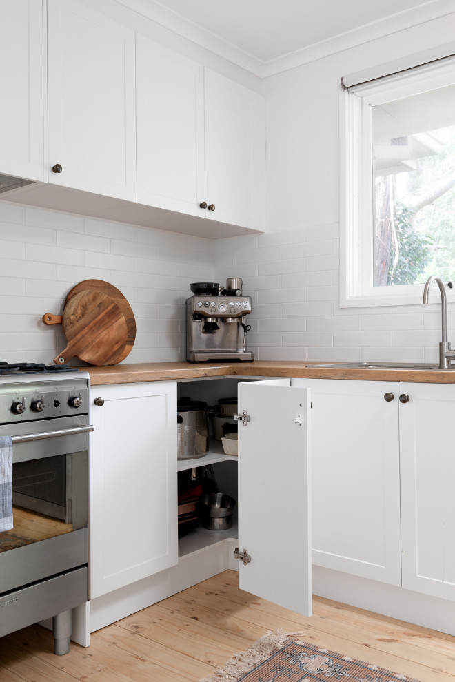 Large scandinavian u-shaped kitchen pantry in Melbourne with a drop-in sink, shaker cabinets, white cabinets, laminate benchtops, white splashback, subway tile splashback, stainless steel appliances and light hardwood floors.