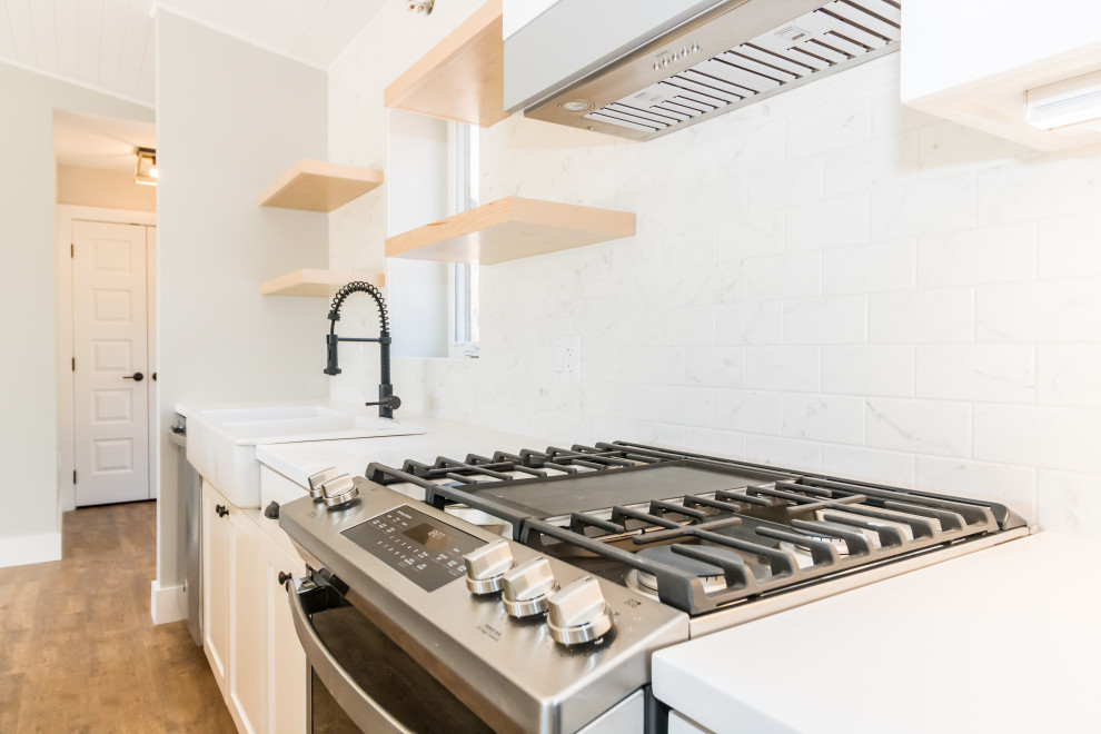 Example of a mid-sized galley vinyl floor and brown floor kitchen design with a farmhouse sink, recessed-panel cabinets, white cabinets, quartzite countertops, stainless steel appliances, an island and multicolored countertops