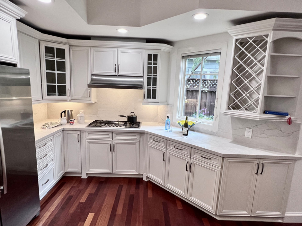 Photo of a mid-sized country u-shaped open plan kitchen in San Francisco with an undermount sink, recessed-panel cabinets, white cabinets, quartz benchtops, white splashback, engineered quartz splashback, stainless steel appliances, dark hardwood floors, with island, brown floor and white benchtop.