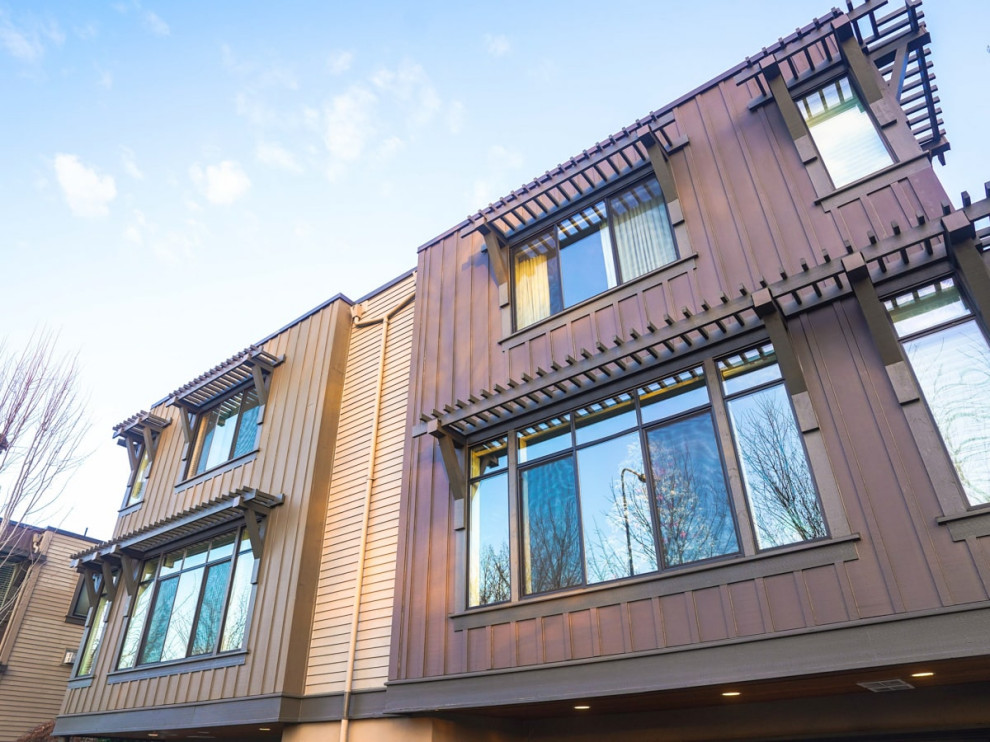 This is an example of a mid-sized modern three-storey stucco brown townhouse exterior in Seattle with a flat roof, a mixed roof, a brown roof and board and batten siding.
