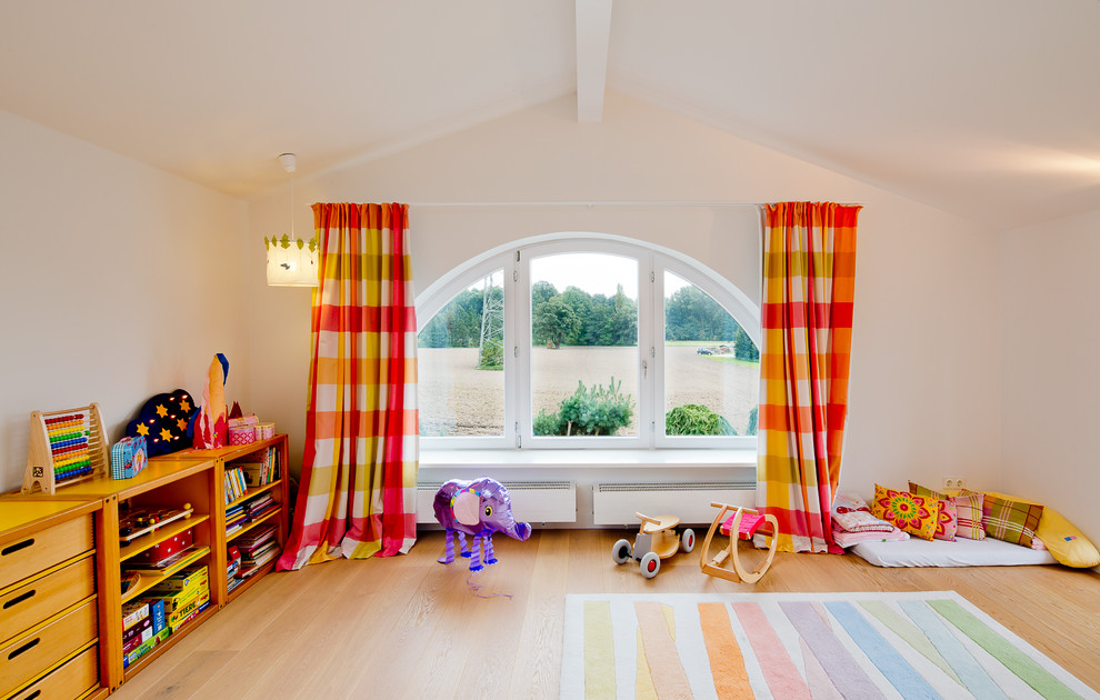 Large contemporary gender-neutral kids' playroom in Dusseldorf with beige walls and light hardwood floors for kids 4-10 years old.