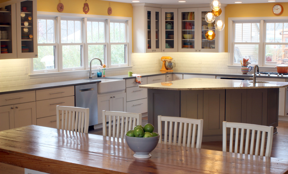 Example of a large transitional l-shaped light wood floor eat-in kitchen design with a farmhouse sink, shaker cabinets, white cabinets, glass countertops, white backsplash, subway tile backsplash, stainless steel appliances and two islands