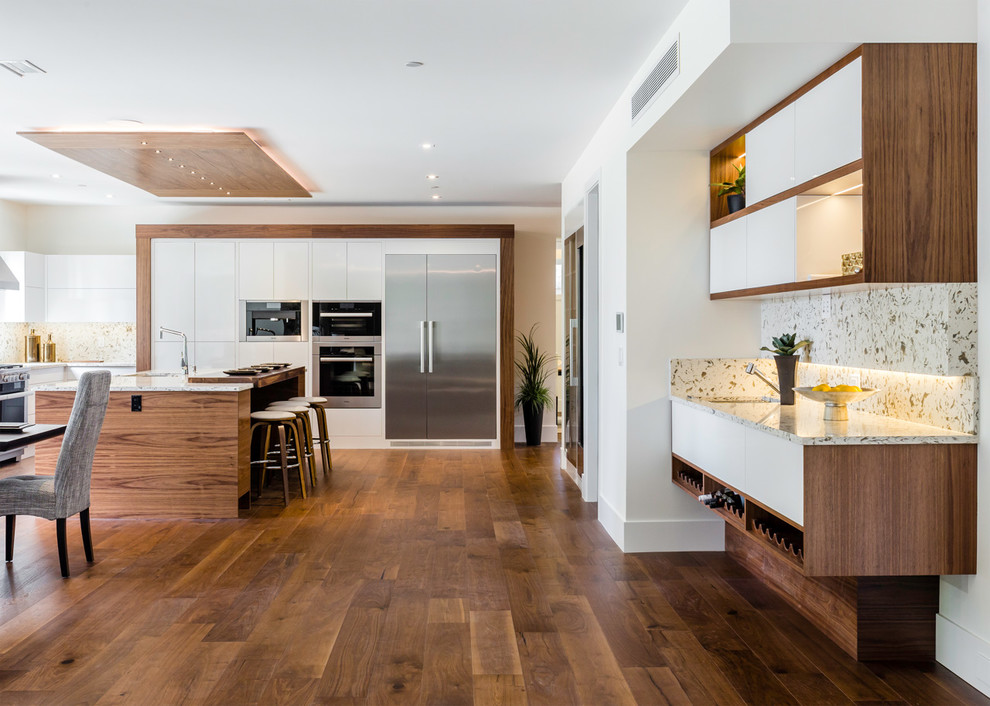 Large contemporary l-shaped eat-in kitchen in Vancouver with an undermount sink, flat-panel cabinets, white cabinets, stone slab splashback, stainless steel appliances, medium hardwood floors, with island and brown floor.