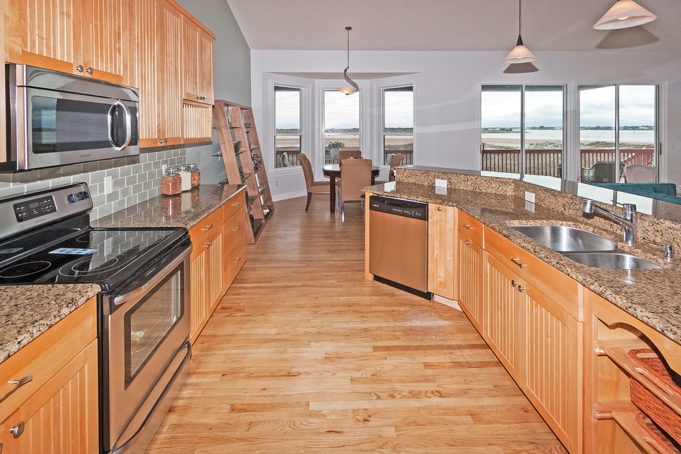 Photo of a mid-sized beach style galley eat-in kitchen in Jacksonville with a double-bowl sink, louvered cabinets, light wood cabinets, granite benchtops, grey splashback, glass tile splashback, stainless steel appliances and light hardwood floors.
