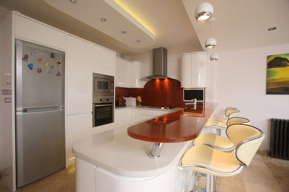 Design ideas for a mid-sized u-shaped eat-in kitchen in London with a double-bowl sink, flat-panel cabinets, white cabinets, granite benchtops, orange splashback, glass sheet splashback, stainless steel appliances, travertine floors, beige floor and white benchtop.