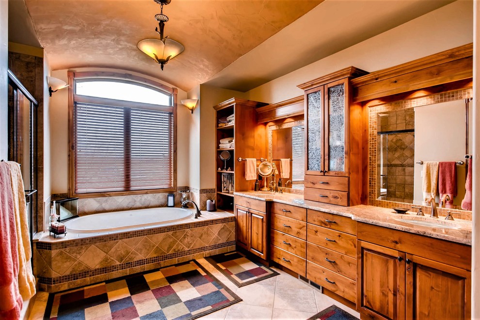 This is an example of an expansive arts and crafts master bathroom in Denver with raised-panel cabinets, medium wood cabinets, an alcove shower, beige tile, beige walls, an undermount sink, beige floor, a sliding shower screen, an alcove tub, mosaic tile, ceramic floors, granite benchtops, beige benchtops, a double vanity, a built-in vanity and vaulted.