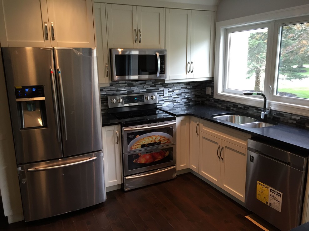 Inspiration for a mid-sized transitional l-shaped dark wood floor and brown floor kitchen remodel in Toronto with an undermount sink, shaker cabinets, white cabinets, multicolored backsplash, matchstick tile backsplash, stainless steel appliances, an island and black countertops