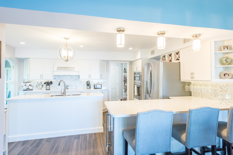 Eat-in kitchen - large transitional u-shaped porcelain tile and brown floor eat-in kitchen idea with an undermount sink, shaker cabinets, white cabinets, quartz countertops, white backsplash, marble backsplash, stainless steel appliances and two islands