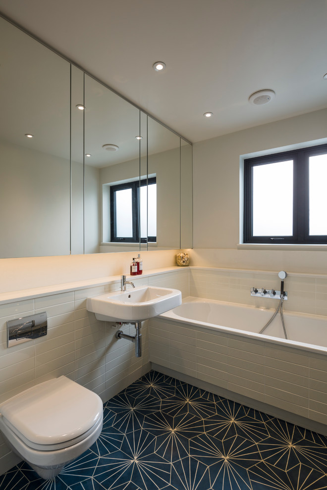 Photo of a scandinavian bathroom in London with engineered quartz benchtops, white tile, a wall-mount toilet, a wall-mount sink and white walls.