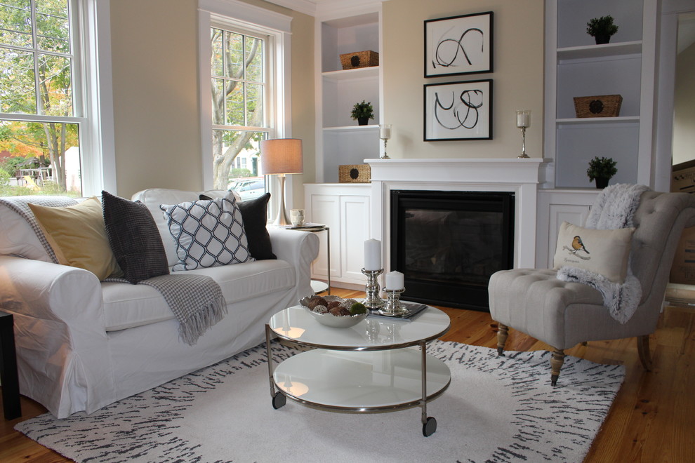 Photo of a small country open concept living room in Boston with beige walls, light hardwood floors, a standard fireplace, a wood fireplace surround, no tv and brown floor.