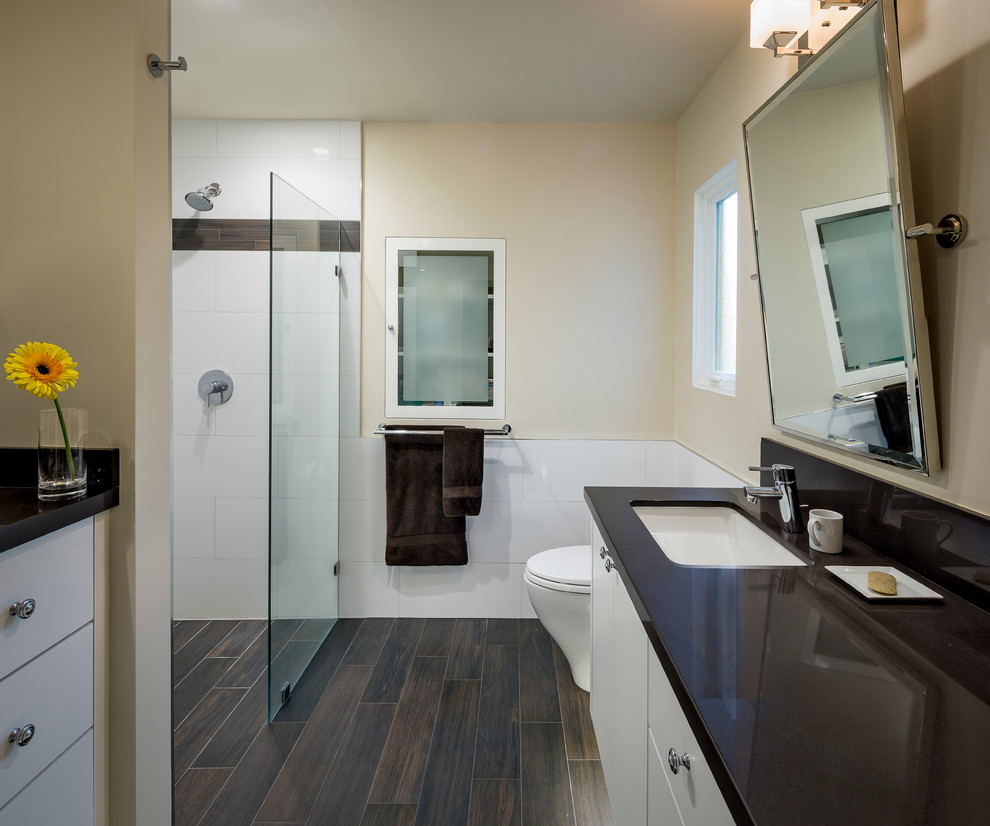 Photo of a mid-sized contemporary 3/4 bathroom in San Francisco with flat-panel cabinets, white cabinets, a curbless shower, a one-piece toilet, white tile, porcelain tile, yellow walls, dark hardwood floors, an undermount sink, solid surface benchtops, brown floor, a hinged shower door, black benchtops, a single vanity, a floating vanity and decorative wall panelling.