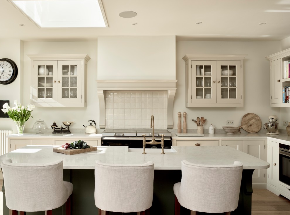Inspiration for a mid-sized traditional l-shaped eat-in kitchen in London with a farmhouse sink, shaker cabinets, white cabinets, quartzite benchtops, white splashback, subway tile splashback, stainless steel appliances, light hardwood floors and with island.