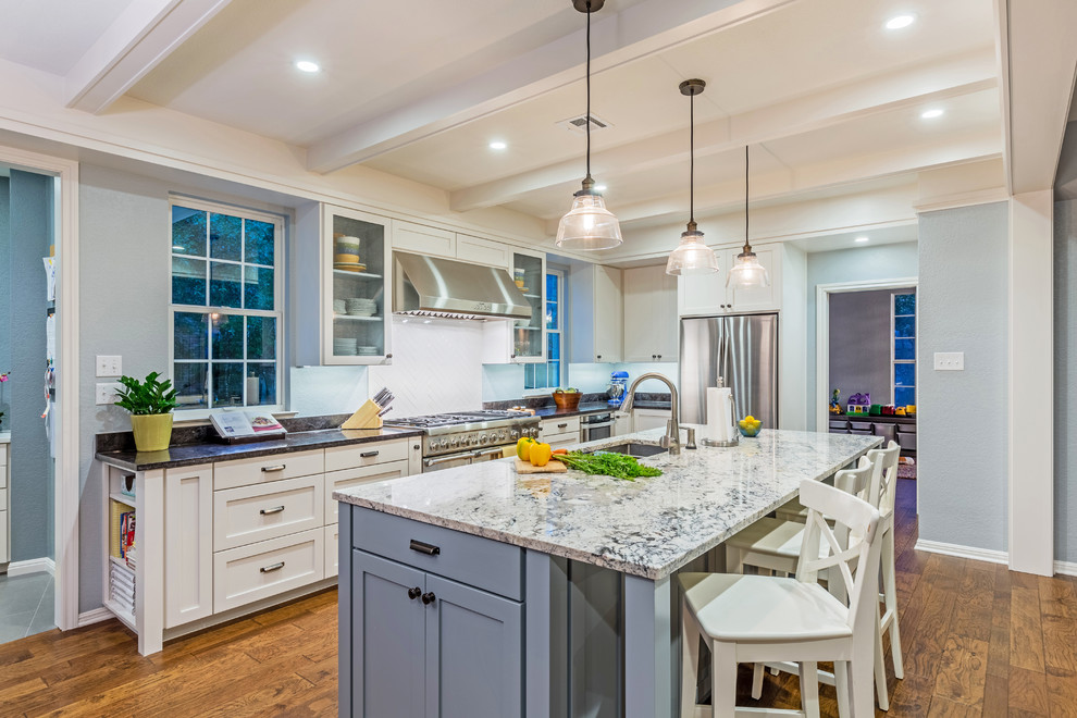 Eat-in kitchen - mid-sized transitional l-shaped medium tone wood floor eat-in kitchen idea in Austin with an undermount sink, shaker cabinets, white cabinets, granite countertops, white backsplash, ceramic backsplash, stainless steel appliances and an island