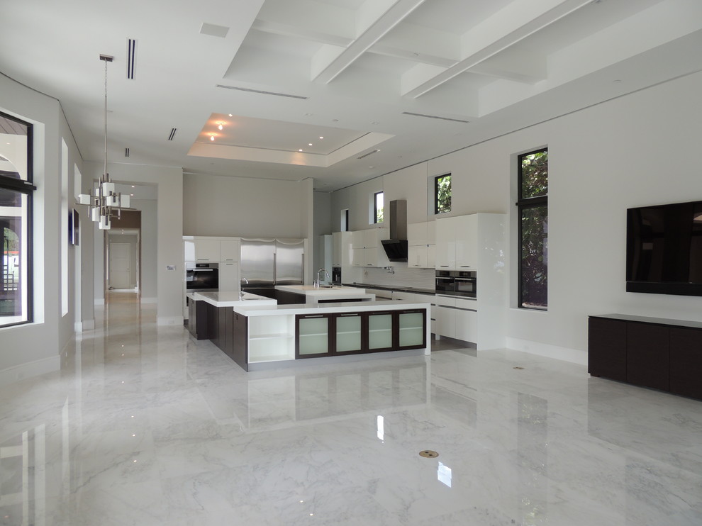 Photo of a large contemporary u-shaped eat-in kitchen in Miami with a double-bowl sink, flat-panel cabinets, white cabinets, quartzite benchtops, white splashback, glass tile splashback, stainless steel appliances, marble floors and multiple islands.