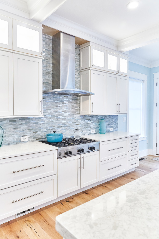 Inspiration for a large transitional l-shaped light wood floor and beige floor open concept kitchen remodel with an undermount sink, shaker cabinets, white cabinets, blue backsplash, matchstick tile backsplash, stainless steel appliances, an island and white countertops