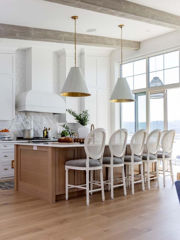 This is an example of a beach style single-wall open plan kitchen in Vancouver with a belfast sink, shaker cabinets, light hardwood flooring, an island, beige floors and exposed beams.