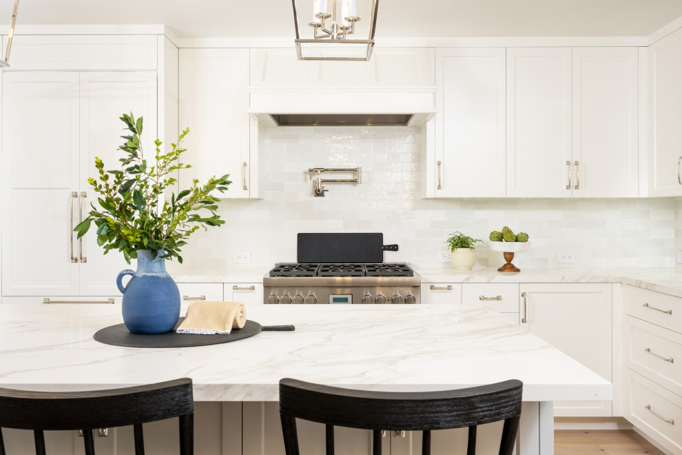Large country l-shaped eat-in kitchen in San Francisco with a farmhouse sink, shaker cabinets, white cabinets, quartz benchtops, white splashback, subway tile splashback, with island, brown floor, white benchtop, panelled appliances and light hardwood floors.