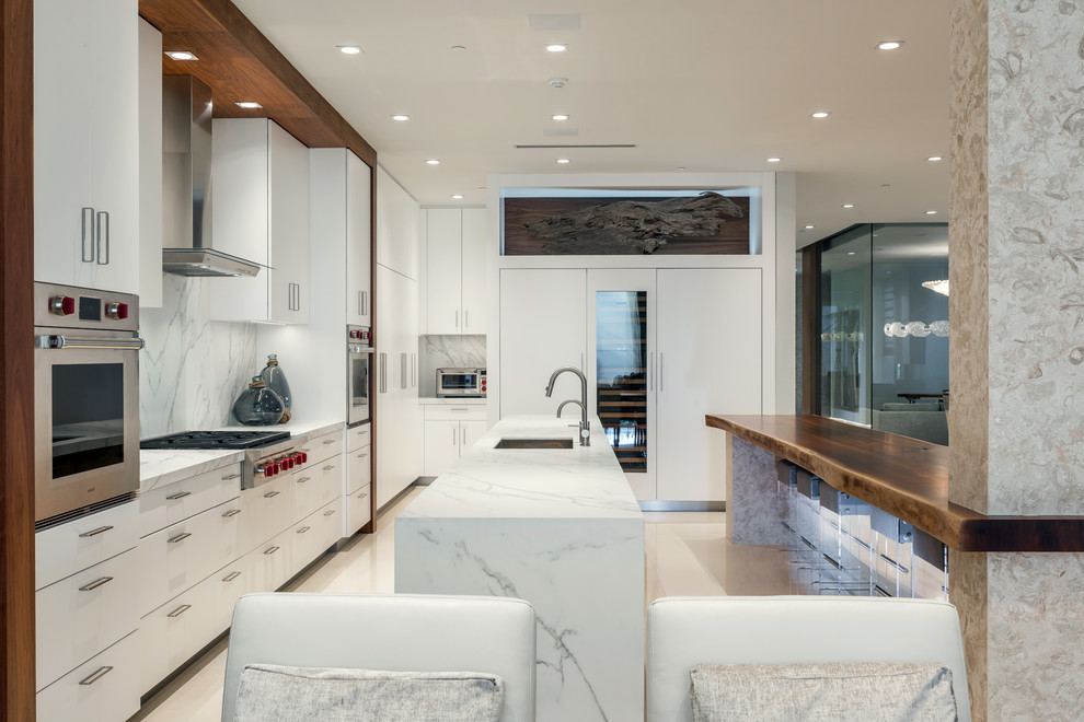 Large contemporary single-wall open plan kitchen in Miami with an undermount sink, flat-panel cabinets, white cabinets, marble benchtops, white splashback, marble splashback, panelled appliances, limestone floors, multiple islands and beige floor.