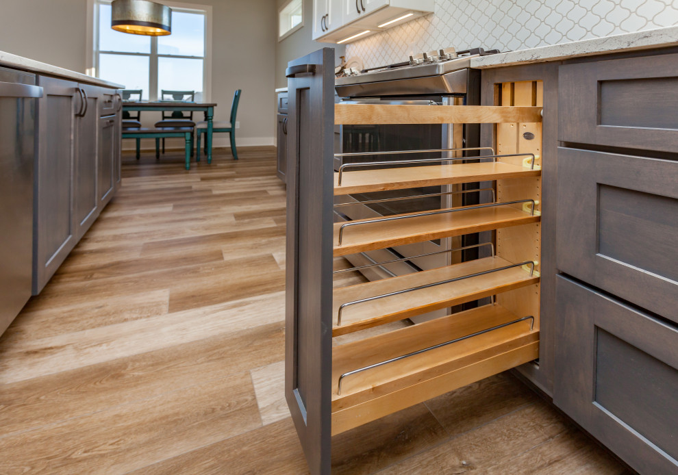 Inspiration for a mid-sized transitional l-shaped light wood floor and brown floor open concept kitchen remodel with an undermount sink, shaker cabinets, white cabinets, quartz countertops, white backsplash, ceramic backsplash, stainless steel appliances, an island and white countertops