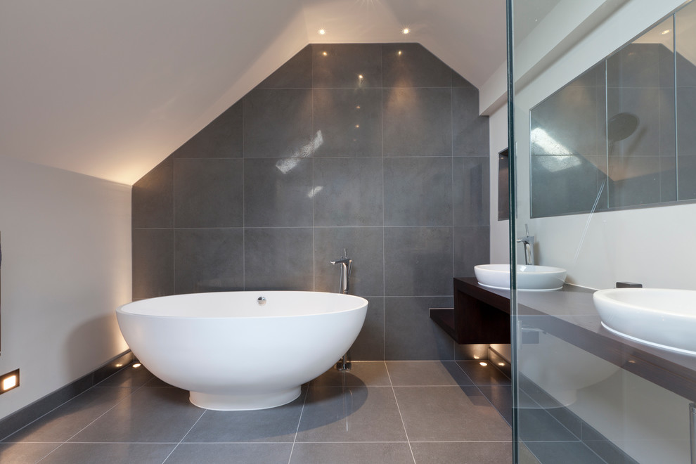 This is an example of a contemporary bathroom in London with a vessel sink, wood benchtops, a freestanding tub, gray tile, white walls and brown benchtops.
