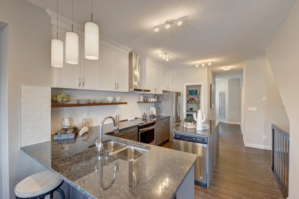Mid-sized transitional l-shaped vinyl floor and black floor eat-in kitchen photo in Edmonton with an undermount sink, shaker cabinets, gray cabinets, granite countertops, white backsplash, subway tile backsplash, stainless steel appliances and an island