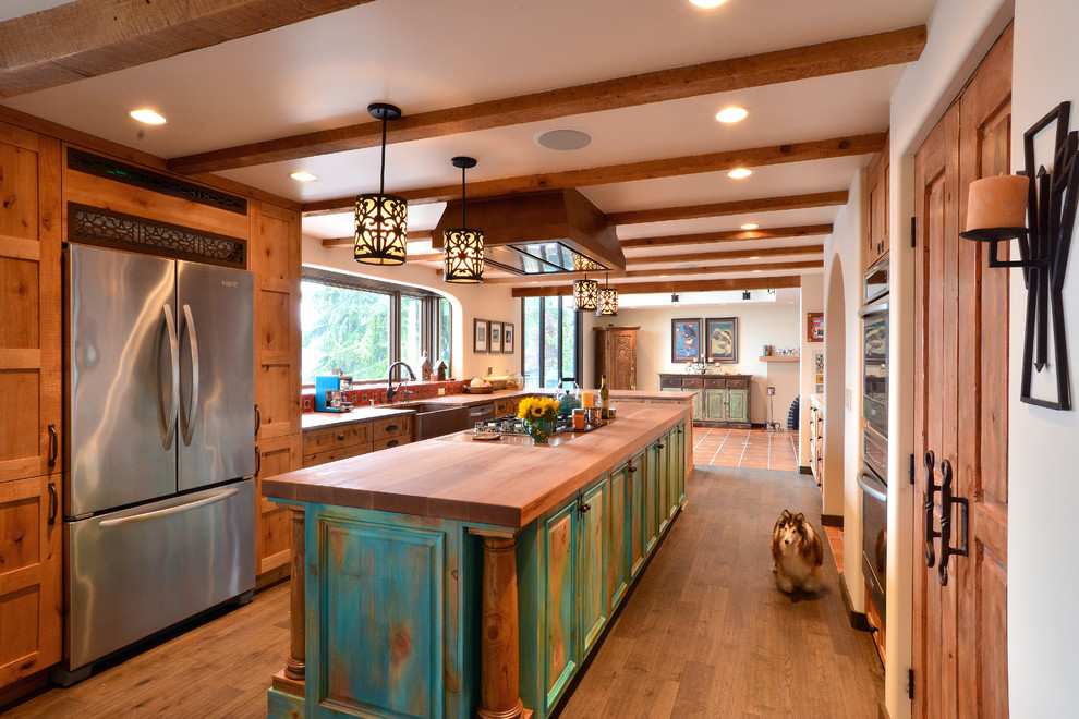 Large l-shaped open plan kitchen in Seattle with a farmhouse sink, recessed-panel cabinets, turquoise cabinets, wood benchtops, multi-coloured splashback, ceramic splashback, stainless steel appliances, medium hardwood floors, with island and brown floor.