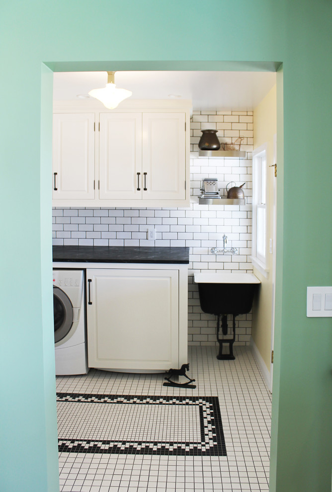 Design ideas for a mid-sized country single-wall dedicated laundry room in Los Angeles with a farmhouse sink, raised-panel cabinets, white cabinets, soapstone benchtops, ceramic floors and beige walls.