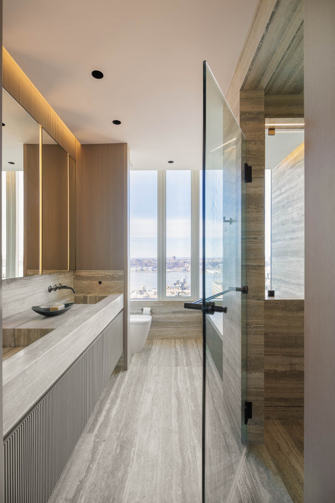 This is an example of a medium sized contemporary ensuite bathroom in New York with raised-panel cabinets, beige cabinets, a corner bath, an alcove shower, a wall mounted toilet, beige tiles, marble tiles, beige walls, marble flooring, an integrated sink, marble worktops, beige floors, a hinged door, beige worktops, double sinks and a floating vanity unit.