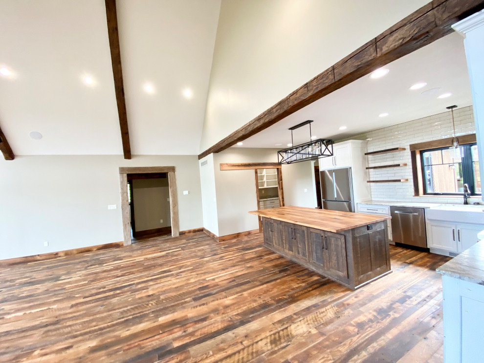 Photo of a medium sized rustic l-shaped open plan kitchen in Kansas City with a belfast sink, shaker cabinets, dark wood cabinets, wood worktops, white splashback, tonge and groove splashback, stainless steel appliances, medium hardwood flooring, an island, brown floors and brown worktops.