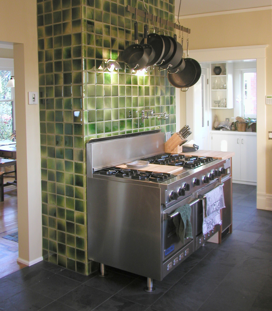 Photo of a mid-sized transitional galley eat-in kitchen in Seattle with stainless steel appliances, a drop-in sink, flat-panel cabinets, mosaic tile splashback, ceramic floors, with island, medium wood cabinets, stainless steel benchtops, beige splashback and black floor.