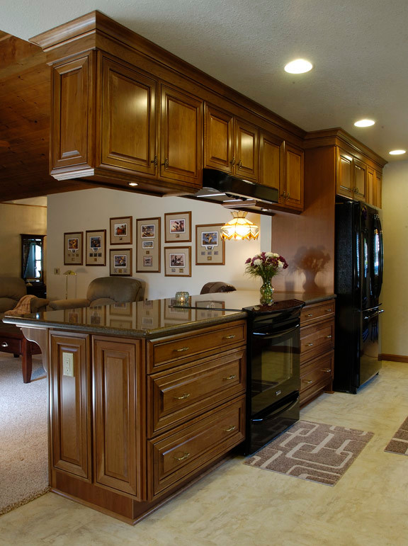 This is an example of a mid-sized traditional galley kitchen in Sacramento with an undermount sink, raised-panel cabinets, medium wood cabinets, recycled glass benchtops, beige splashback, stone tile splashback, black appliances, porcelain floors and no island.