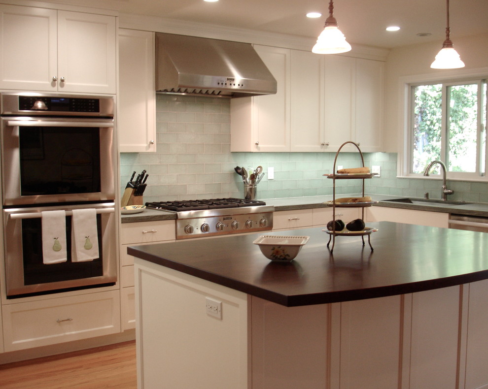 This is an example of a mid-sized traditional l-shaped open plan kitchen in San Francisco with a drop-in sink, shaker cabinets, white cabinets, green splashback, light hardwood floors, with island, granite benchtops, glass tile splashback, stainless steel appliances, brown floor and green benchtop.