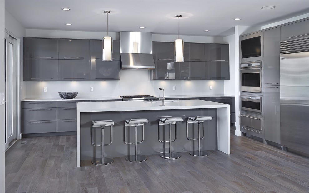 Photo of a large contemporary l-shaped eat-in kitchen in Edmonton with an undermount sink, flat-panel cabinets, grey cabinets, quartz benchtops, white splashback, glass sheet splashback, stainless steel appliances, medium hardwood floors and with island.