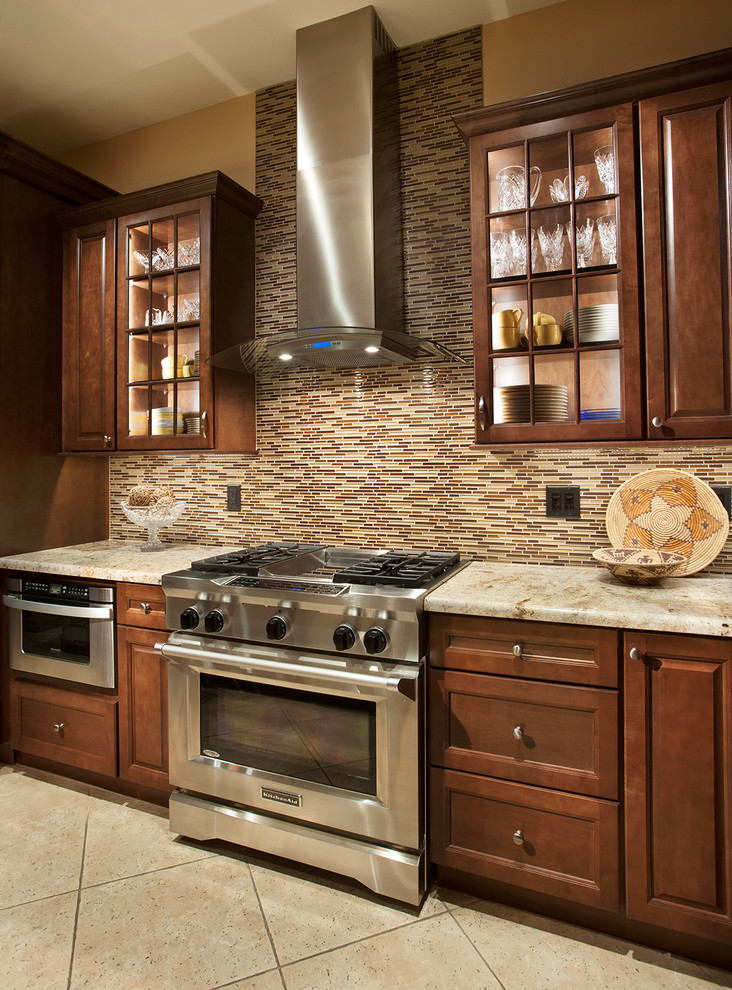Mid-sized transitional single-wall travertine floor eat-in kitchen photo in Phoenix with beaded inset cabinets, medium tone wood cabinets, solid surface countertops, beige backsplash, glass tile backsplash, stainless steel appliances and an island