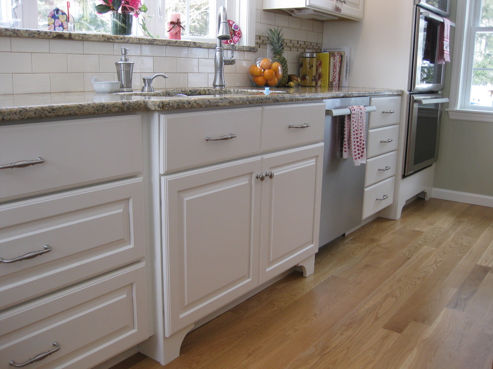 Transitional u-shaped medium tone wood floor eat-in kitchen photo in Boston with an undermount sink, raised-panel cabinets, white cabinets, granite countertops, white backsplash, ceramic backsplash, stainless steel appliances, an island and beige countertops